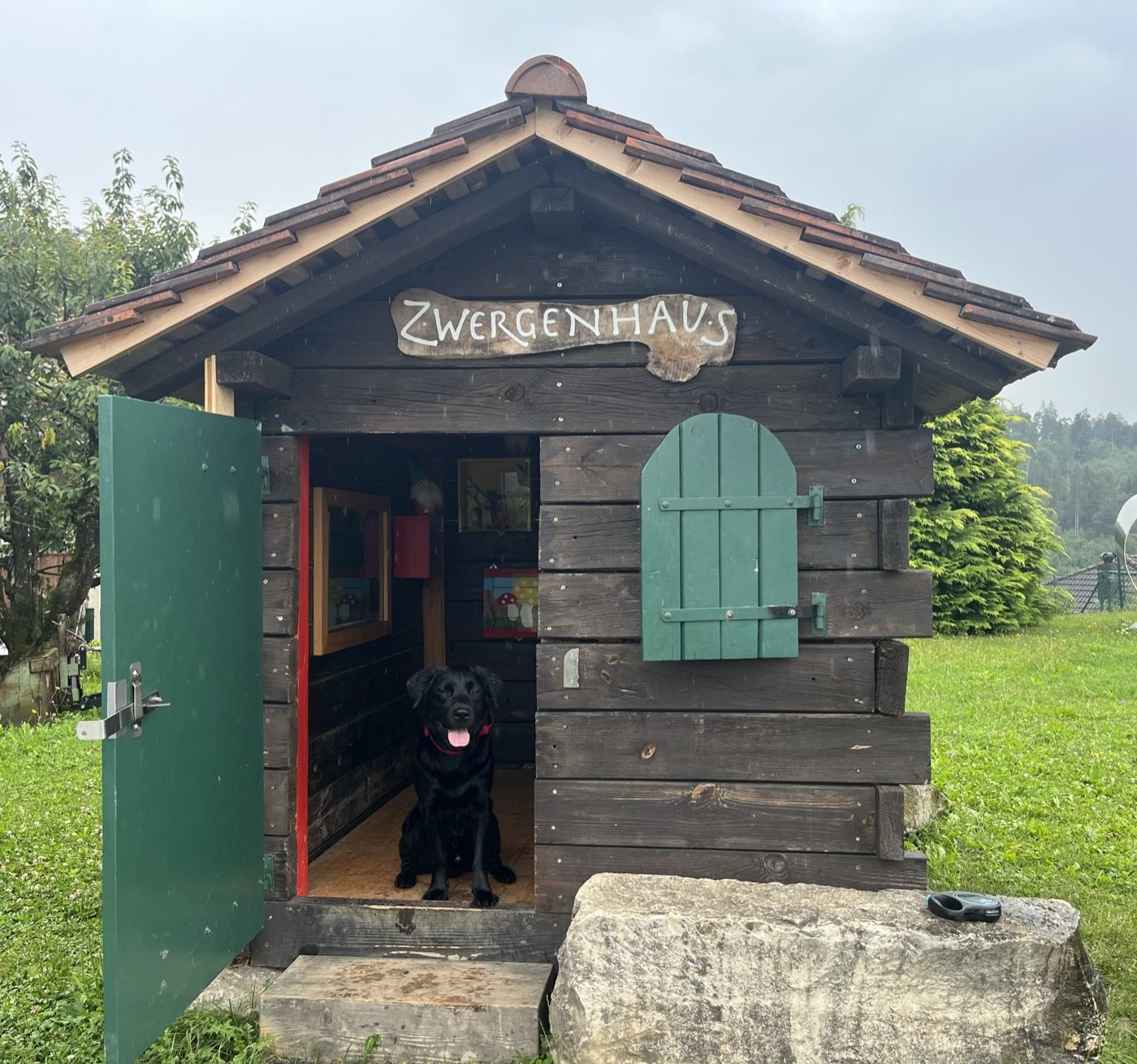 Nino steht in der offenen Tür eines kleinen Holzhauses mit der Aufschrift „Zwergenhaus“.